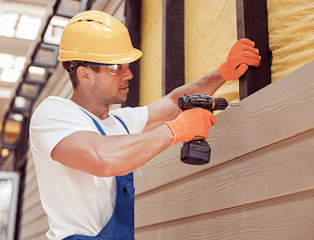 Exterior contractor installing light brown horizontal siding with a power drill