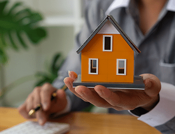 A person's hand holding a small, orange model house