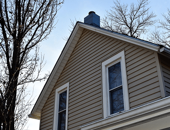 House with light brown siding, white-framed windows, and a metal chimney.